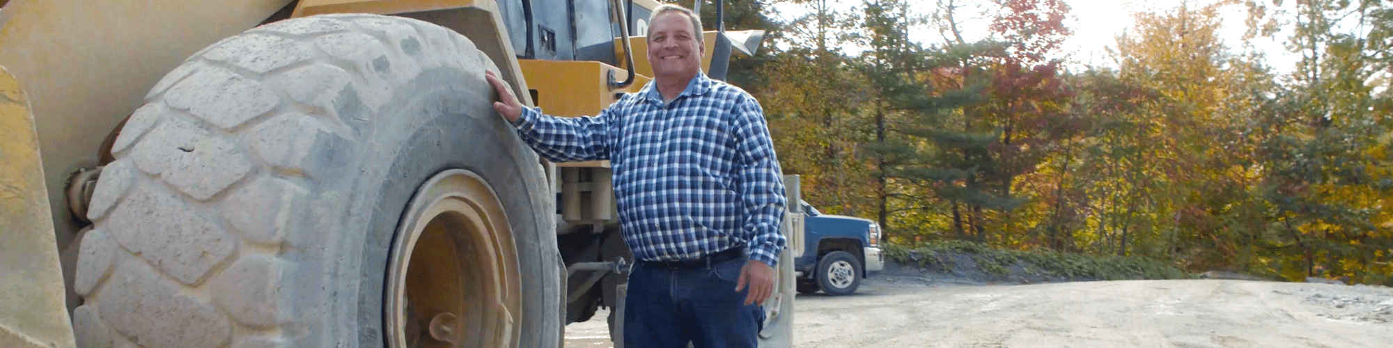 A man smiling while standing next to a bucket loader